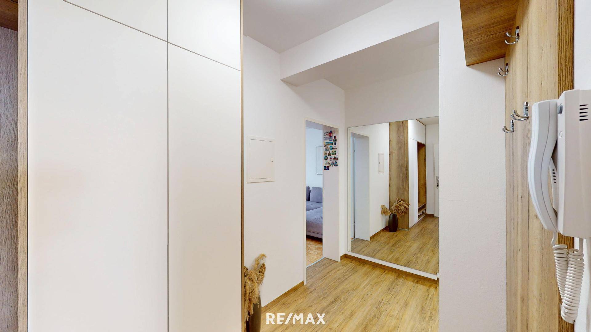 Heller Flur mit Holzfußboden, Garderobe und großem Spiegel.