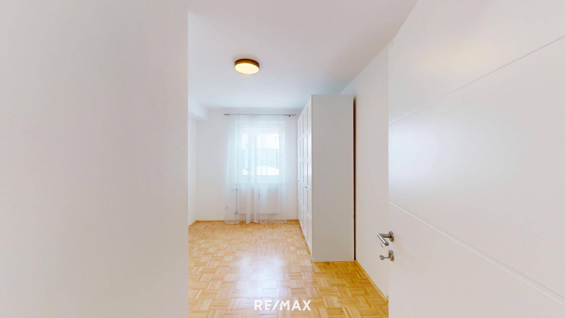 Helles Schlafzimmer mit Parkettboden, Fenster und weißem Kleiderschrank.