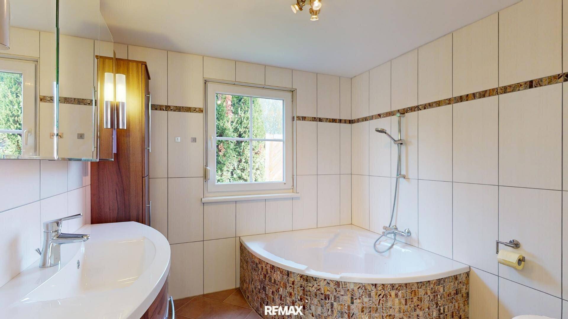 Badezimmer mit Eckbadewanne, Einzelwaschbecken und hellen Fliesen an den Wänden.