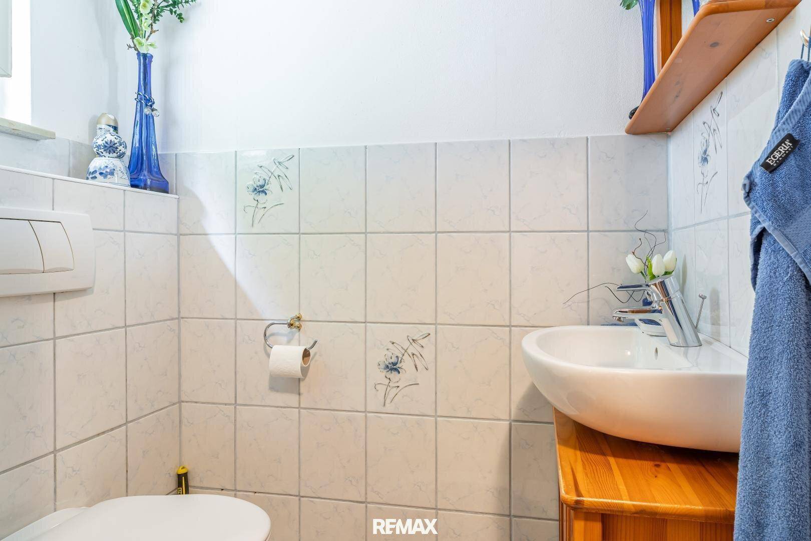 Kleines Gäste-WC mit weißen Fliesen, Einzelwaschbecken und blauen Dekorationsakzenten.