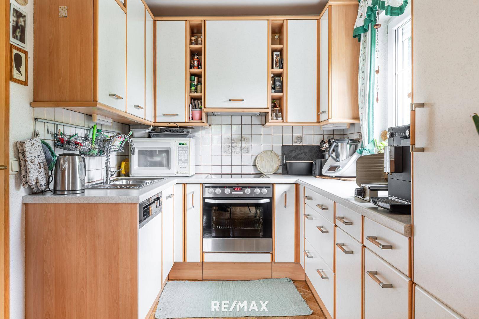 Funktionale Küche mit hellen Holz- und weißen Schränken, ausgestattet mit Standardgeräten und Fliesenboden.