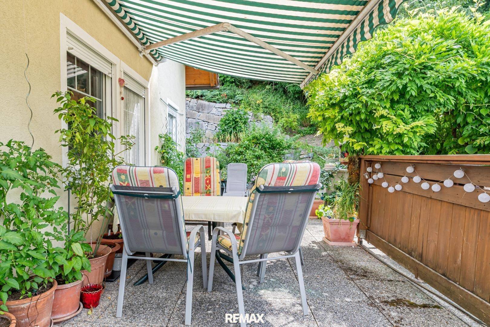 Gemütliche Terrasse mit Markise, Gartenmöbeln und vielen Topfpflanzen, ideal zum Entspannen.