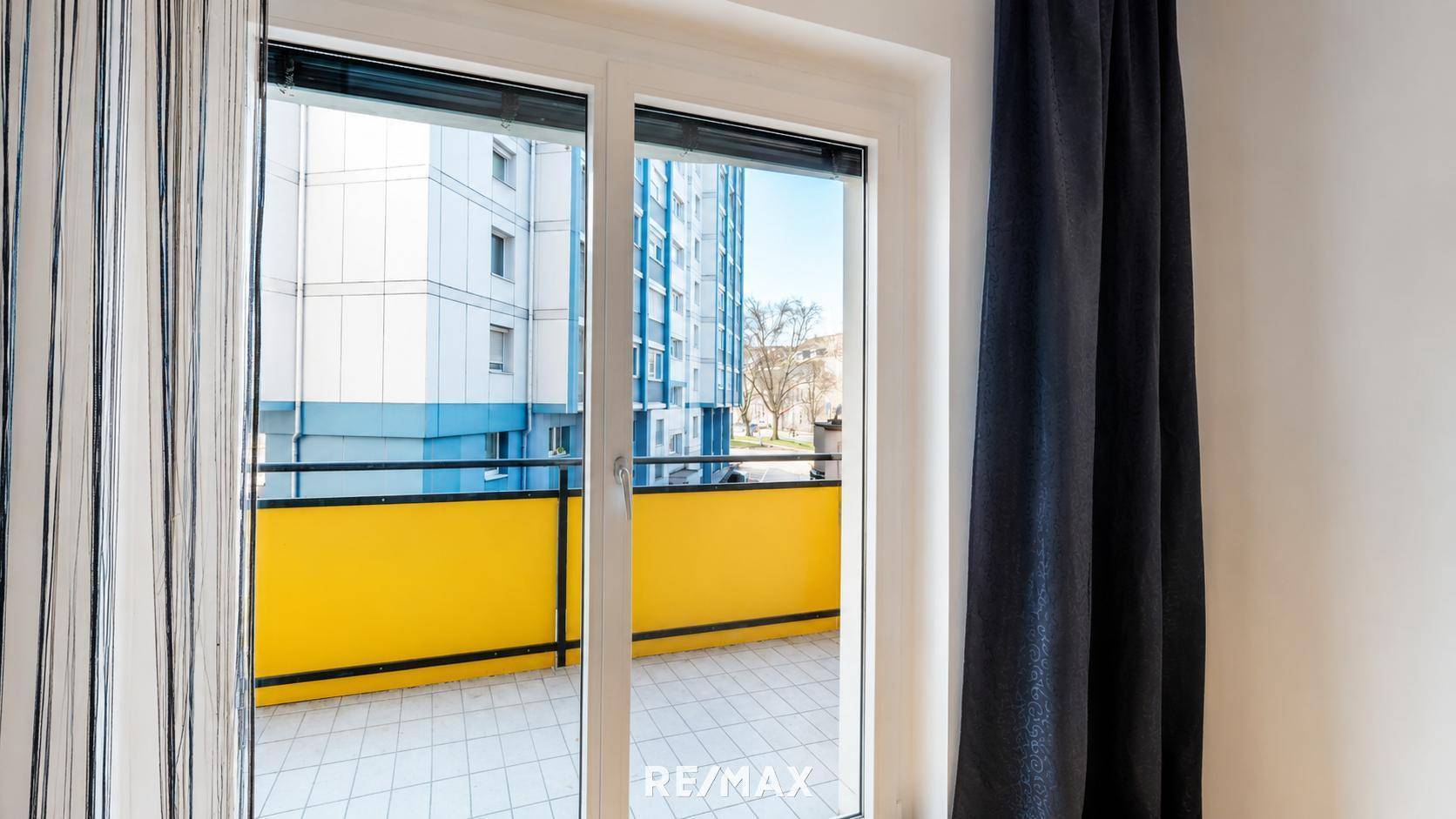Blick vom Innenraum auf den Balkon mit gelbem Geländer und Fliesenboden.