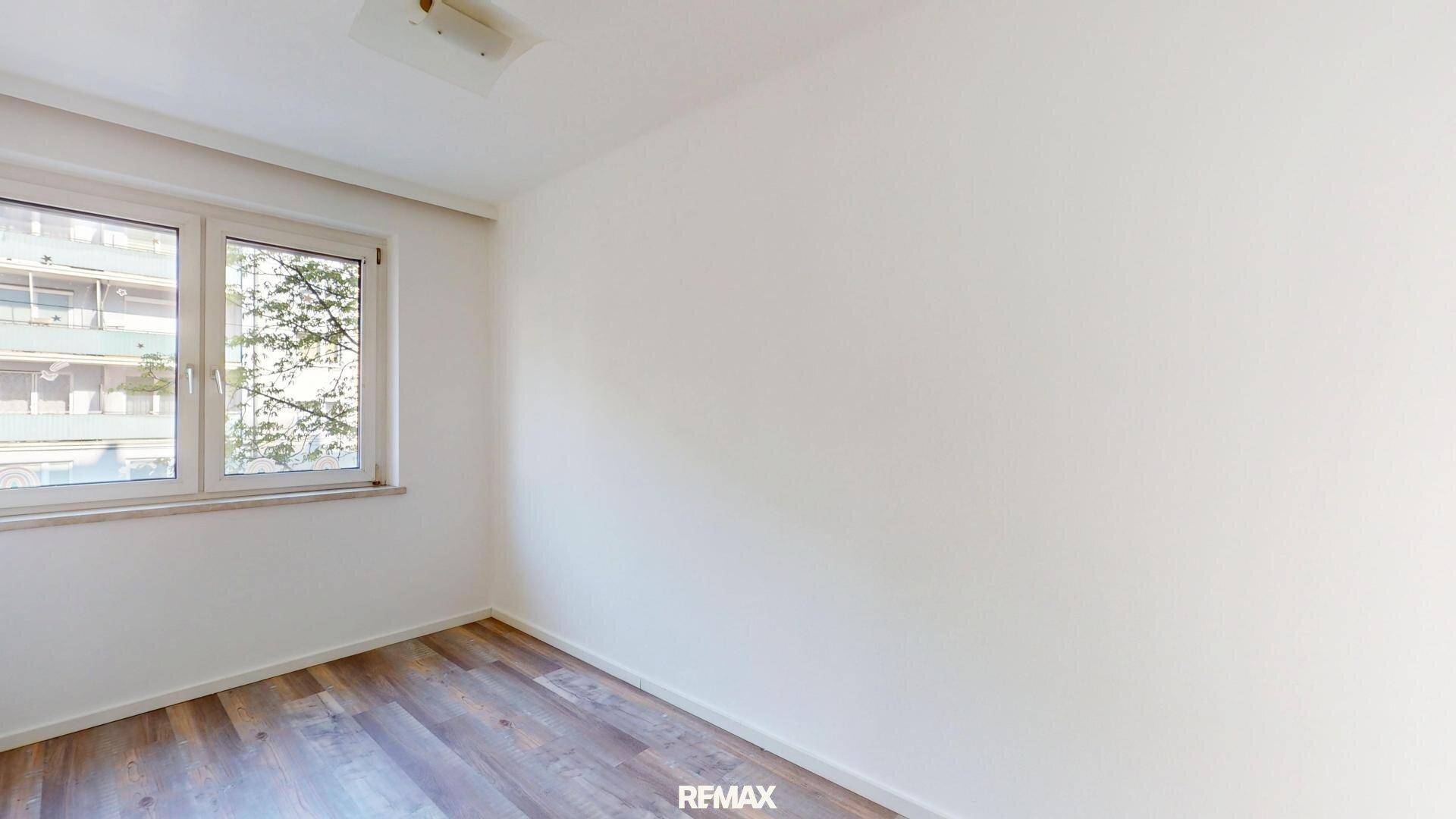 Helles Schlafzimmer mit Laminatboden und Fenster mit Blick ins Grüne.