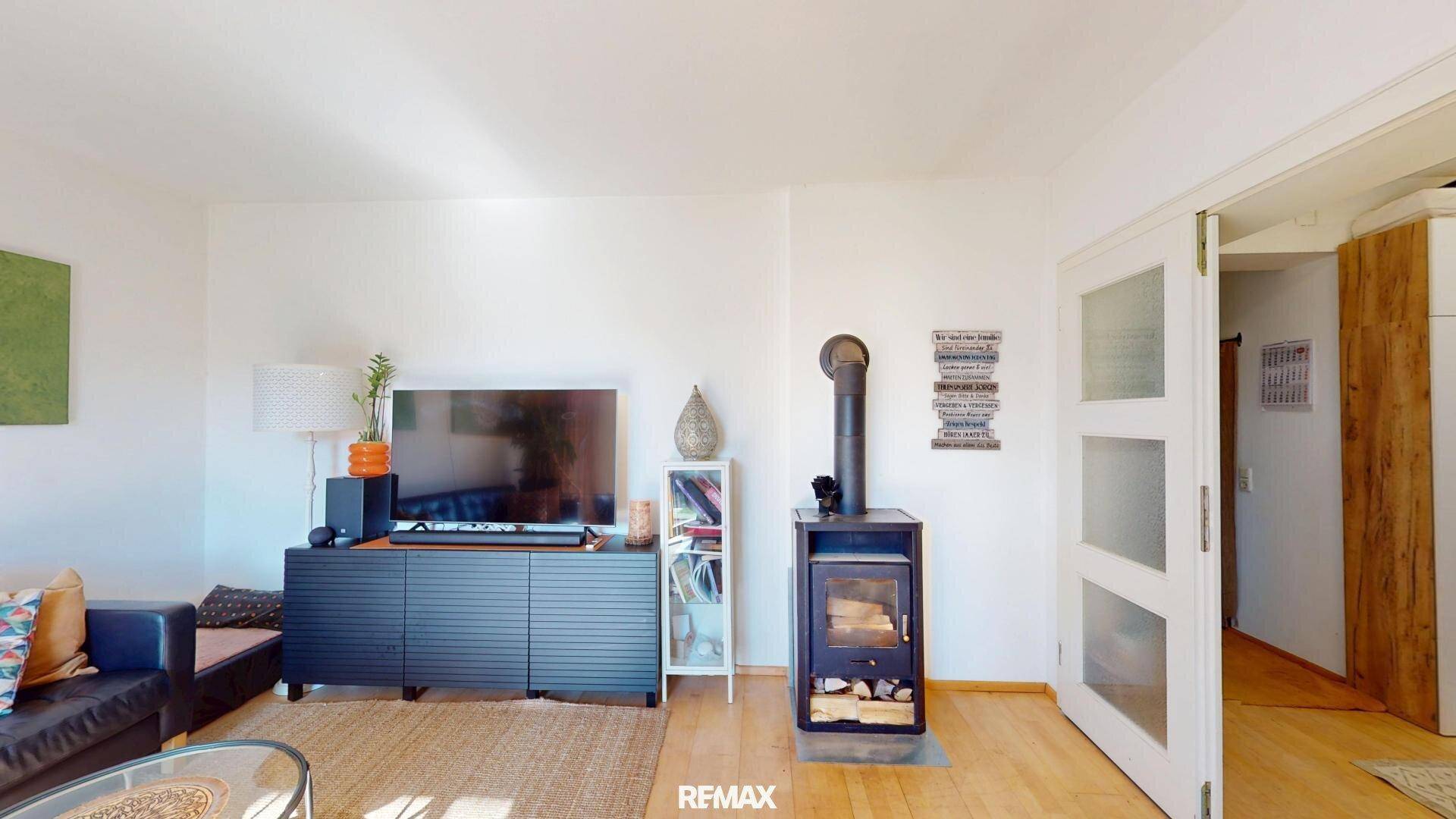 Gemütliches Wohnzimmer mit Holzboden, Fernseher und einem modernen Holzofen.