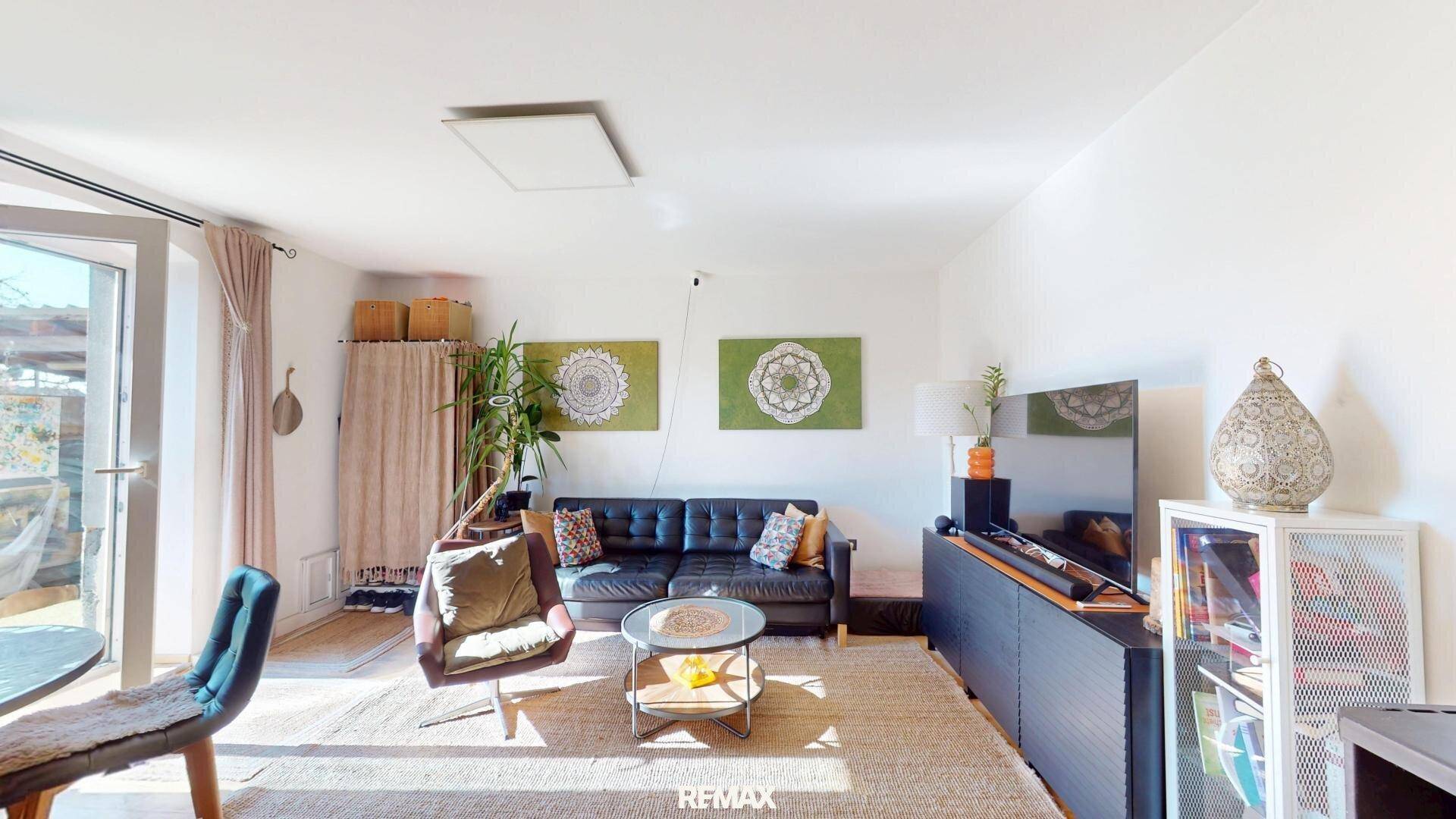 Helles Wohnzimmer mit Sofa, Sessel und Zugang zu einem Außenbereich.