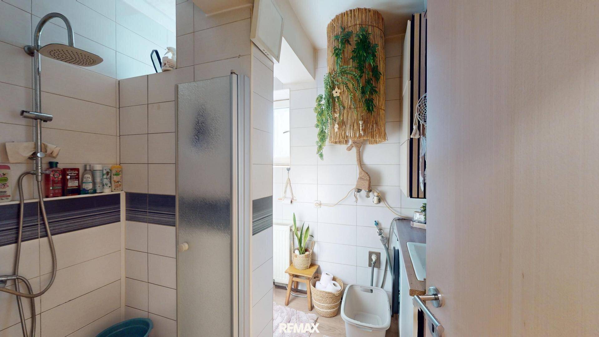 Badezimmer mit Duschkabine, Waschmaschine und Fliesenboden.