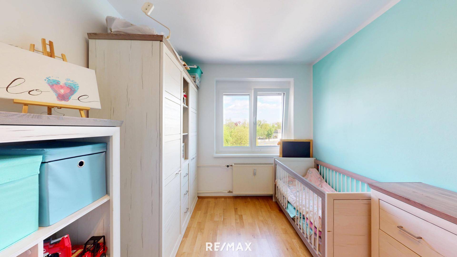 Helles Kinderzimmer mit Holzboden, Babybett und farbiger Wandgestaltung.