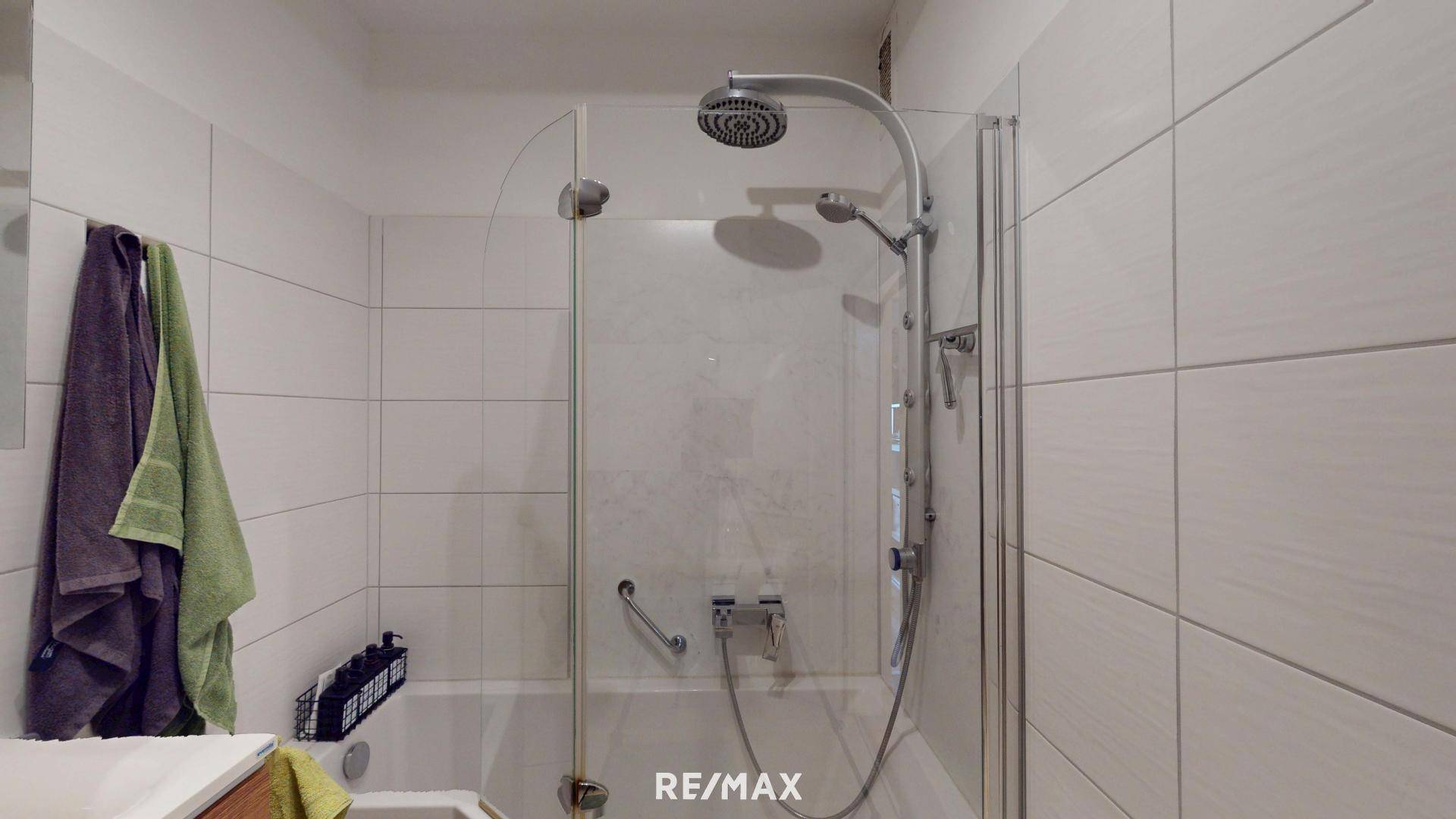 Duschbereich über der Badewanne mit Glasabtrennung und weißen Wandfliesen.
