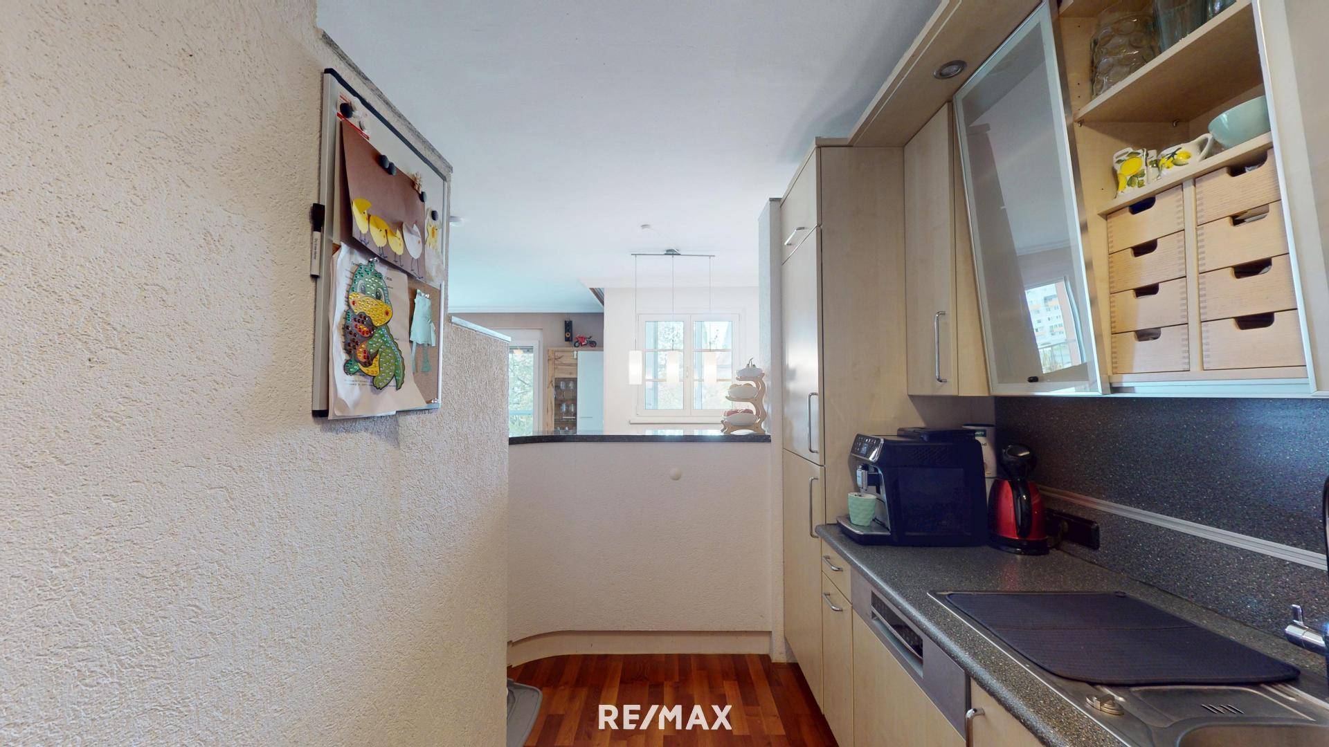 Funktionale Küche mit hellen Holzfronten, dunkler Arbeitsplatte und Durchreiche zum Wohnbereich.