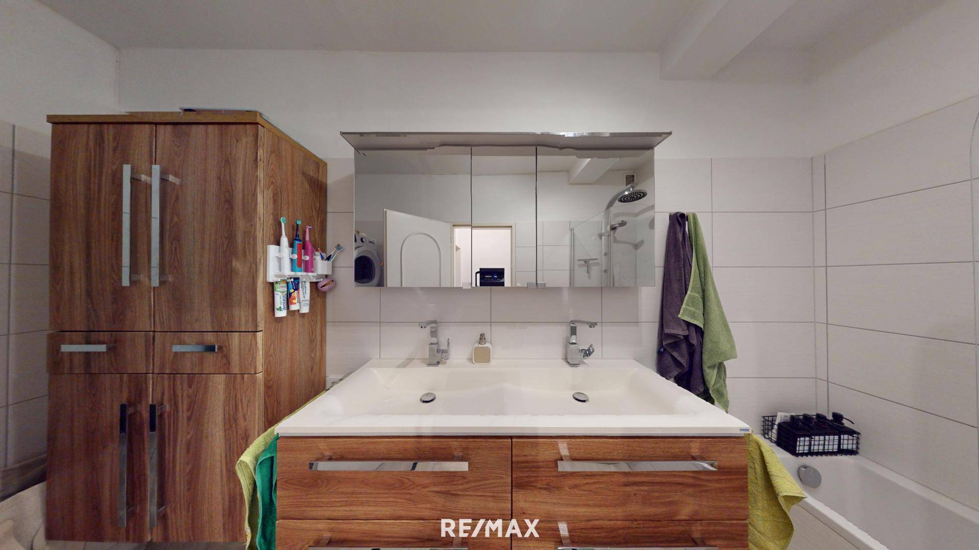 Badezimmer mit Doppelwaschbecken, Holzschränken und weißen Wandfliesen.