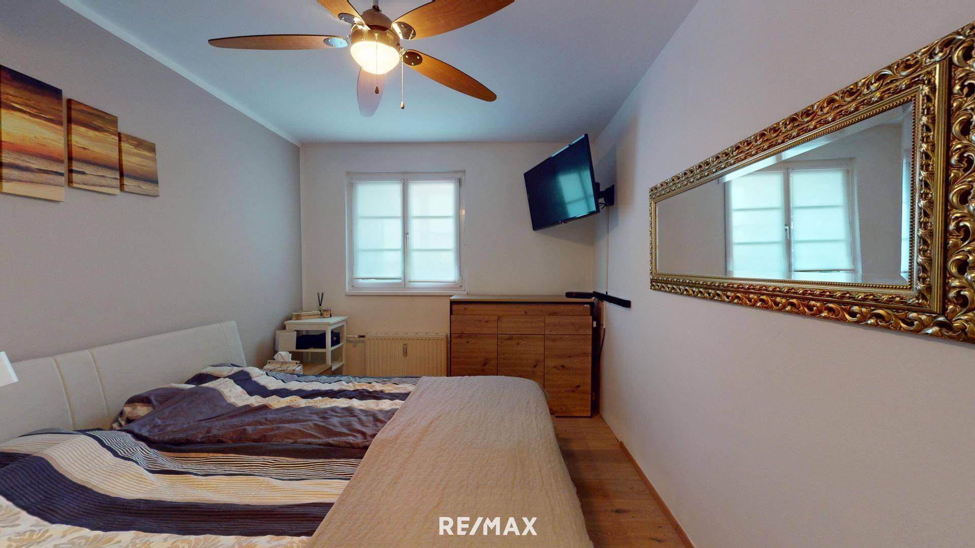 Schlafzimmer mit großem Bett, Deckenventilator und Wandspiegel.