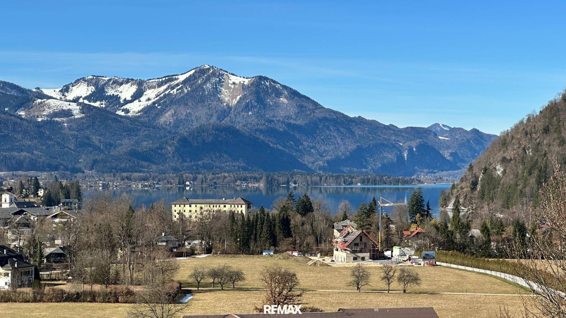 Beeindruckender Ausblick auf den See und schneebedeckte Berge unter blauem Himmel.