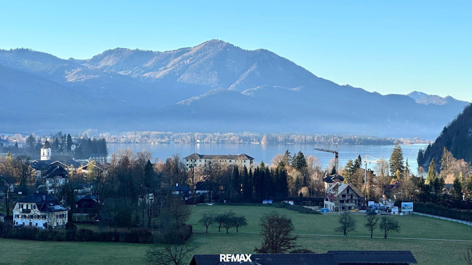 Malerischer Panoramablick auf den Wolfgangsee mit Bergkulisse und Dorfbebauung.