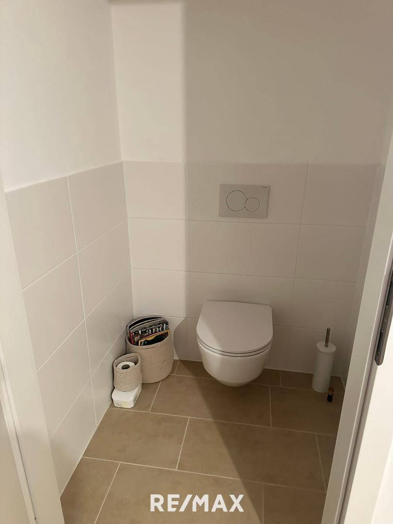 Modernes Gäste-WC mit Wand-WC und hellen Fliesen an Wänden und Boden.