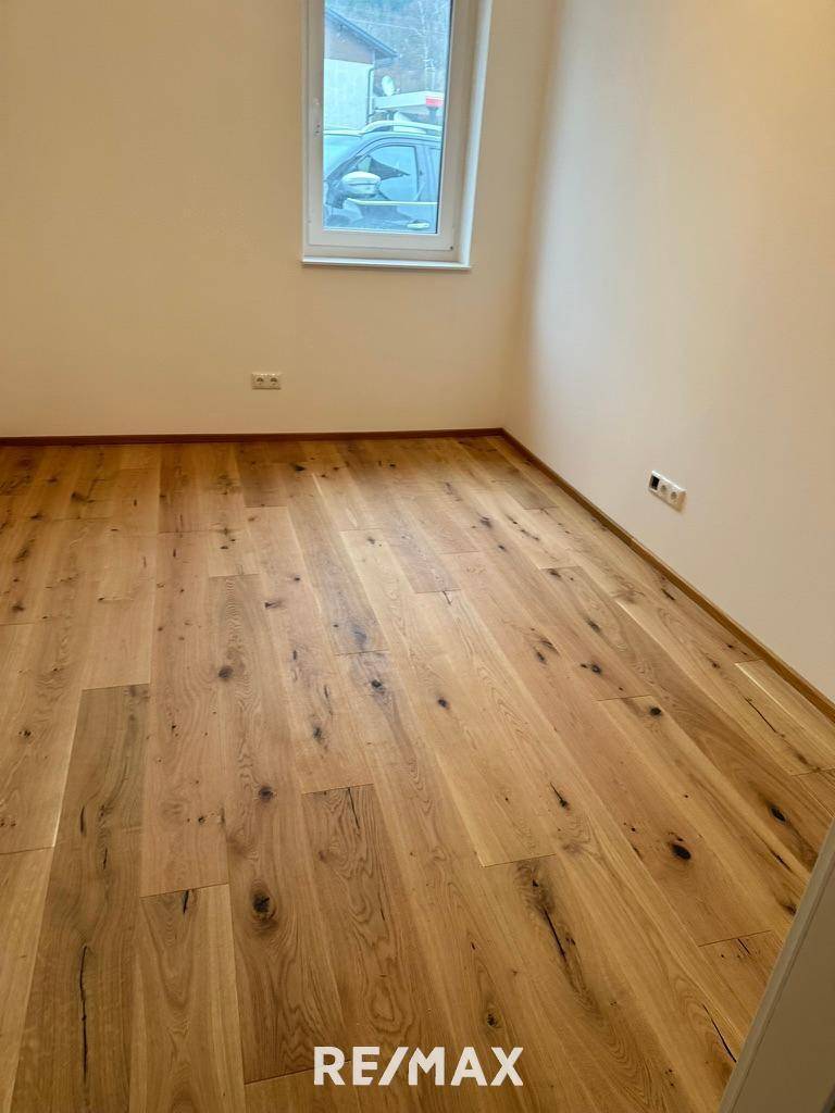 Helles Zimmer mit Holzboden und einem Fenster, das Tageslicht hereinlässt.