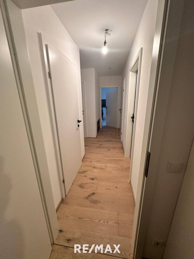 Langer, heller Flur mit Holzboden und weißen Türen, der verschiedene Räume verbindet.