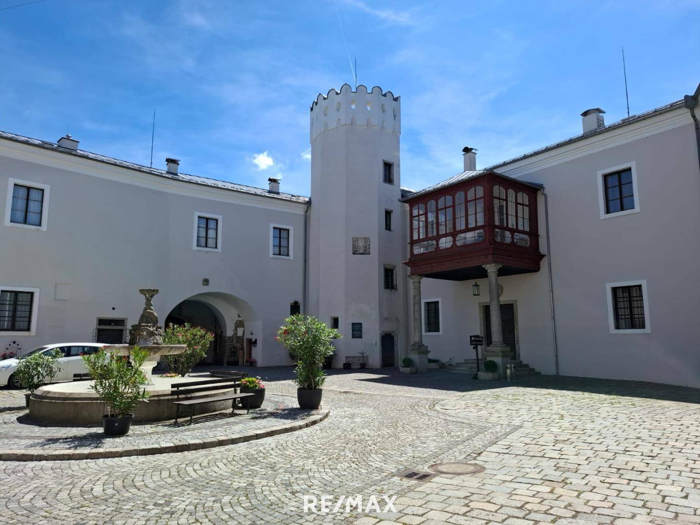 Historisches Gebäude mit Innenhof, Turm und gepflastertem Bereich unter blauem Himmel.