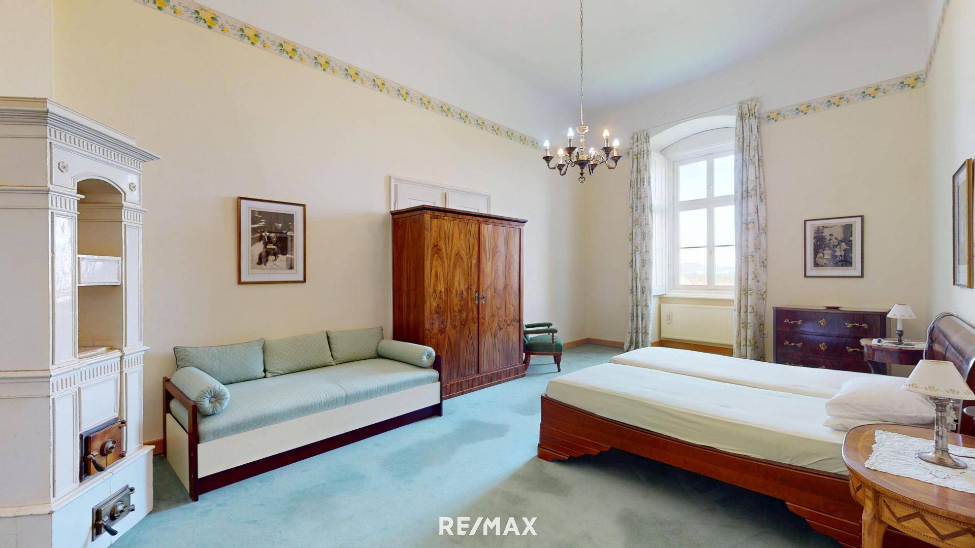 Helles Schlafzimmer mit traditionellem Kachelofen, zwei Einzelbetten und antiken Möbeln.