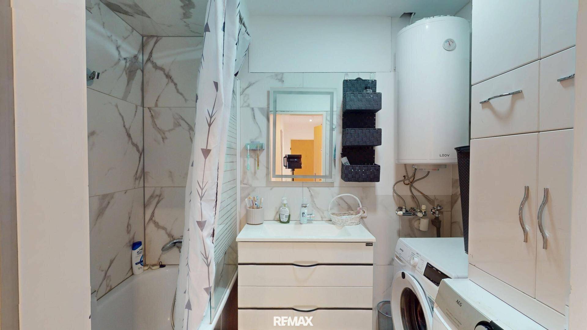 Funktionales Badezimmer mit Badewanne, Waschmaschine und hellen Fliesen.