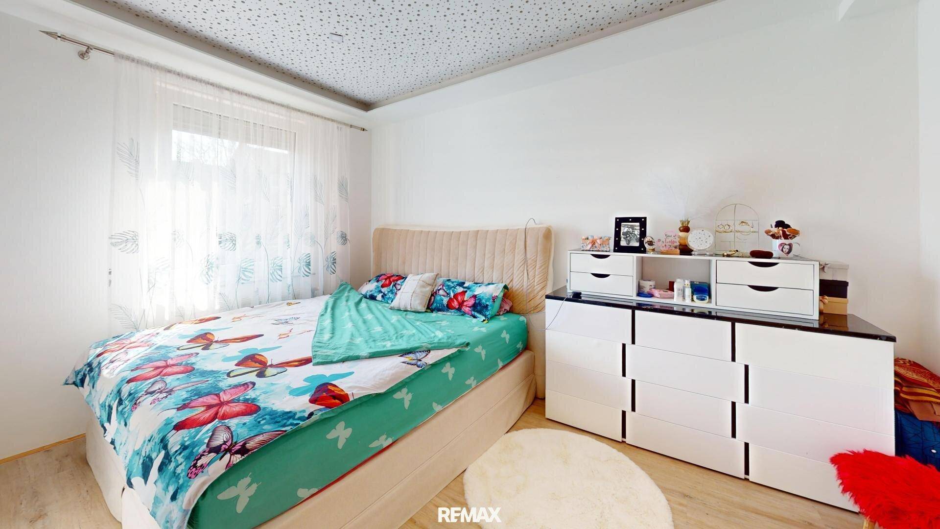 Gemütliches Schlafzimmer mit Doppelbett, Kommode und Fenster mit Vorhängen.