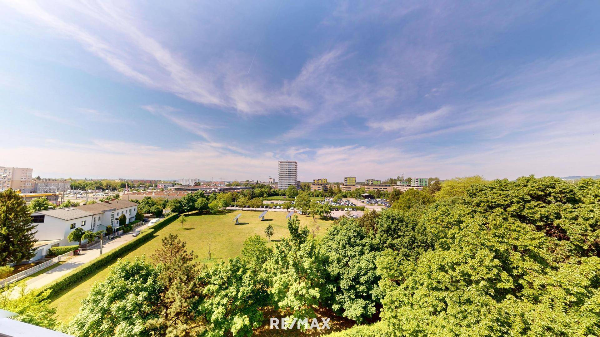 Weitläufiger Blick über grüne Parkanlagen und Wohngebäude unter blauem Himmel.
