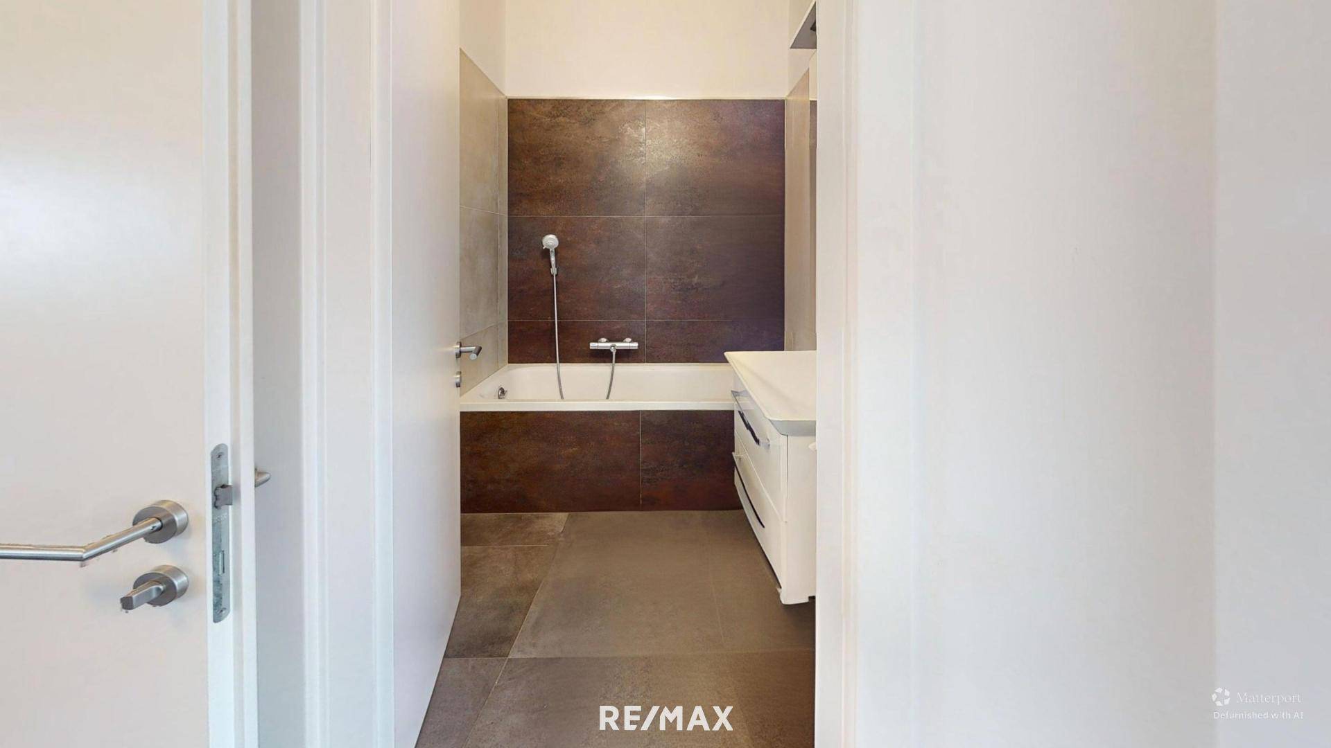 Badezimmer mit Badewanne, Duschfunktion und dunklen Fliesen an der Wand sowie hellem Boden.