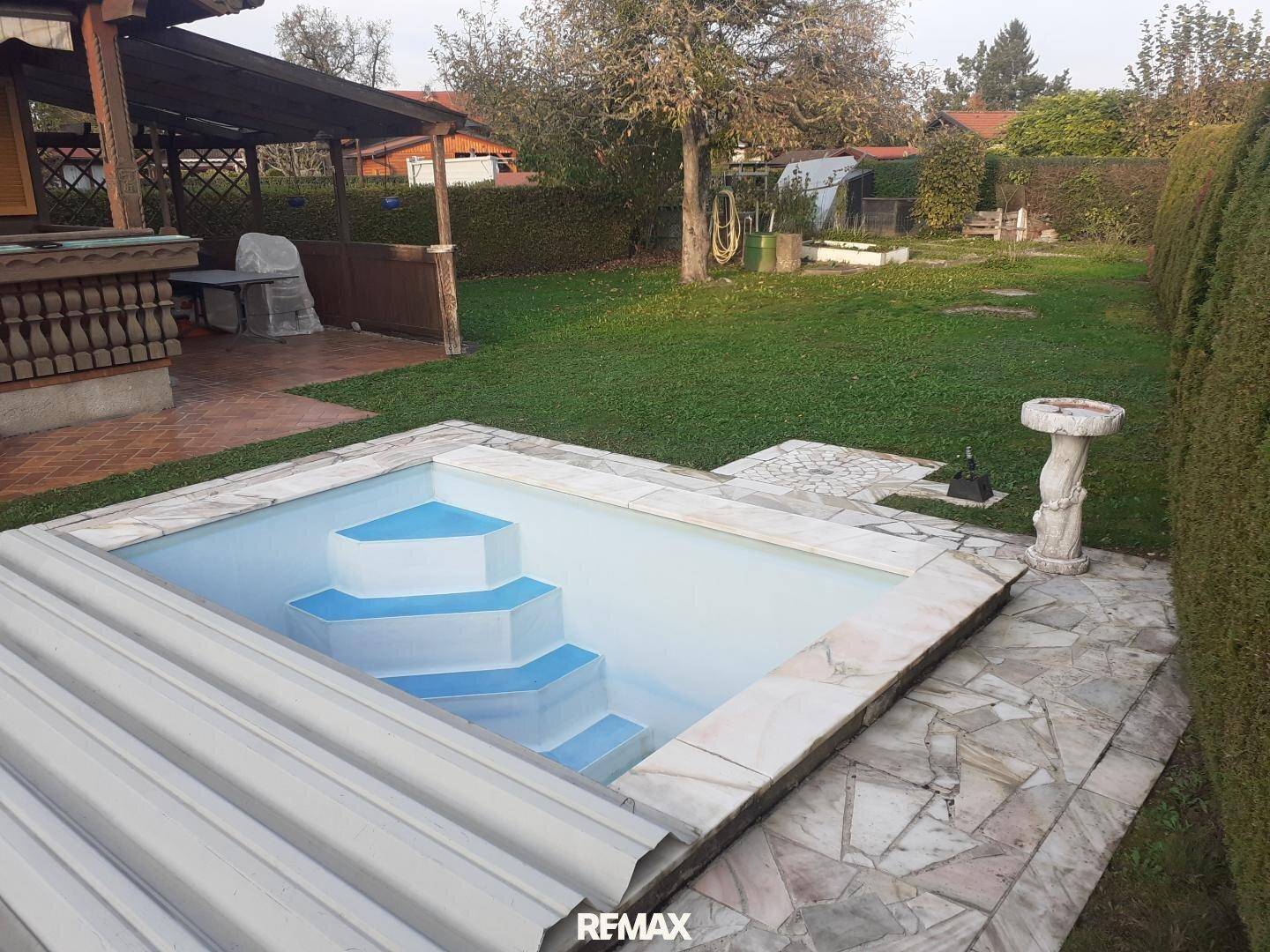 Gartenbereich mit kleinem Pool, Liegefläche und umgebender Hecke.