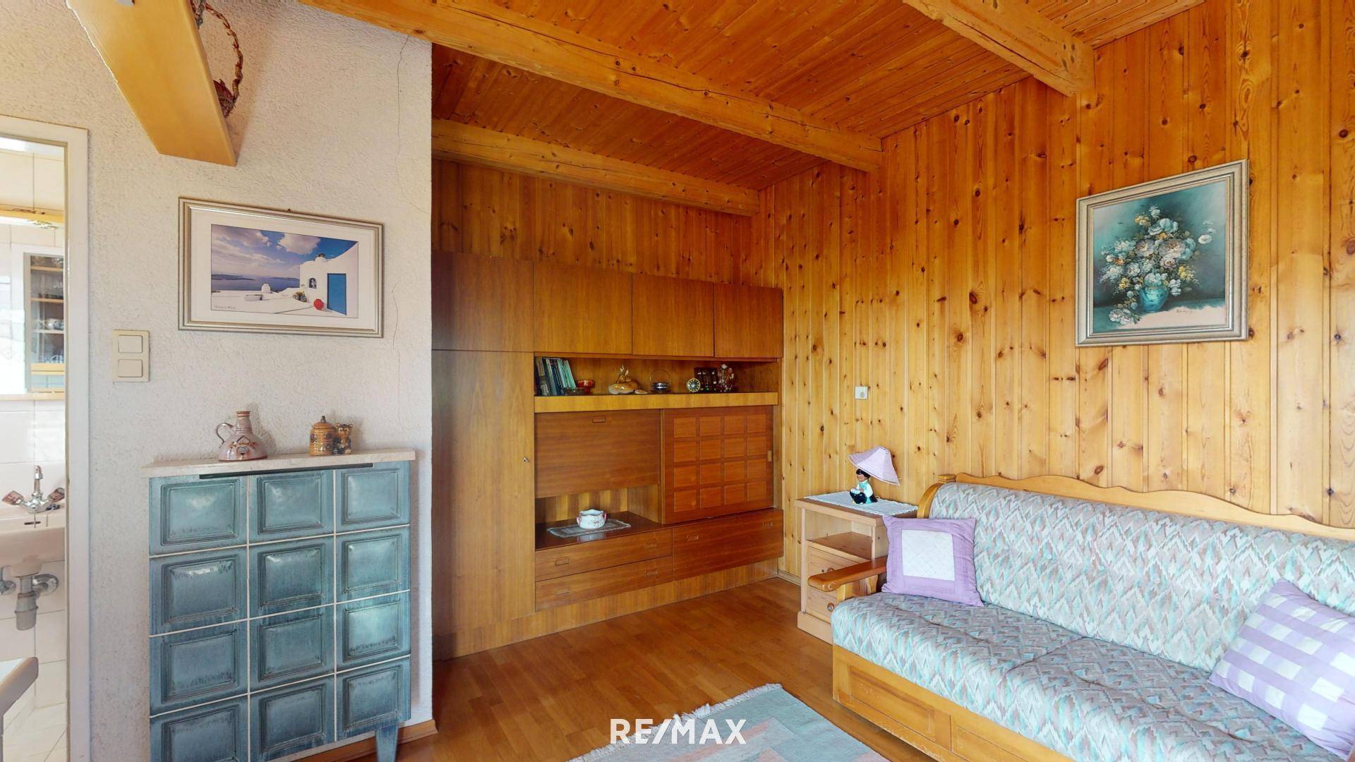 Rustikales Wohnzimmer mit Holzwänden, Sofa, Kachelofen und integrierten Holzregalen.