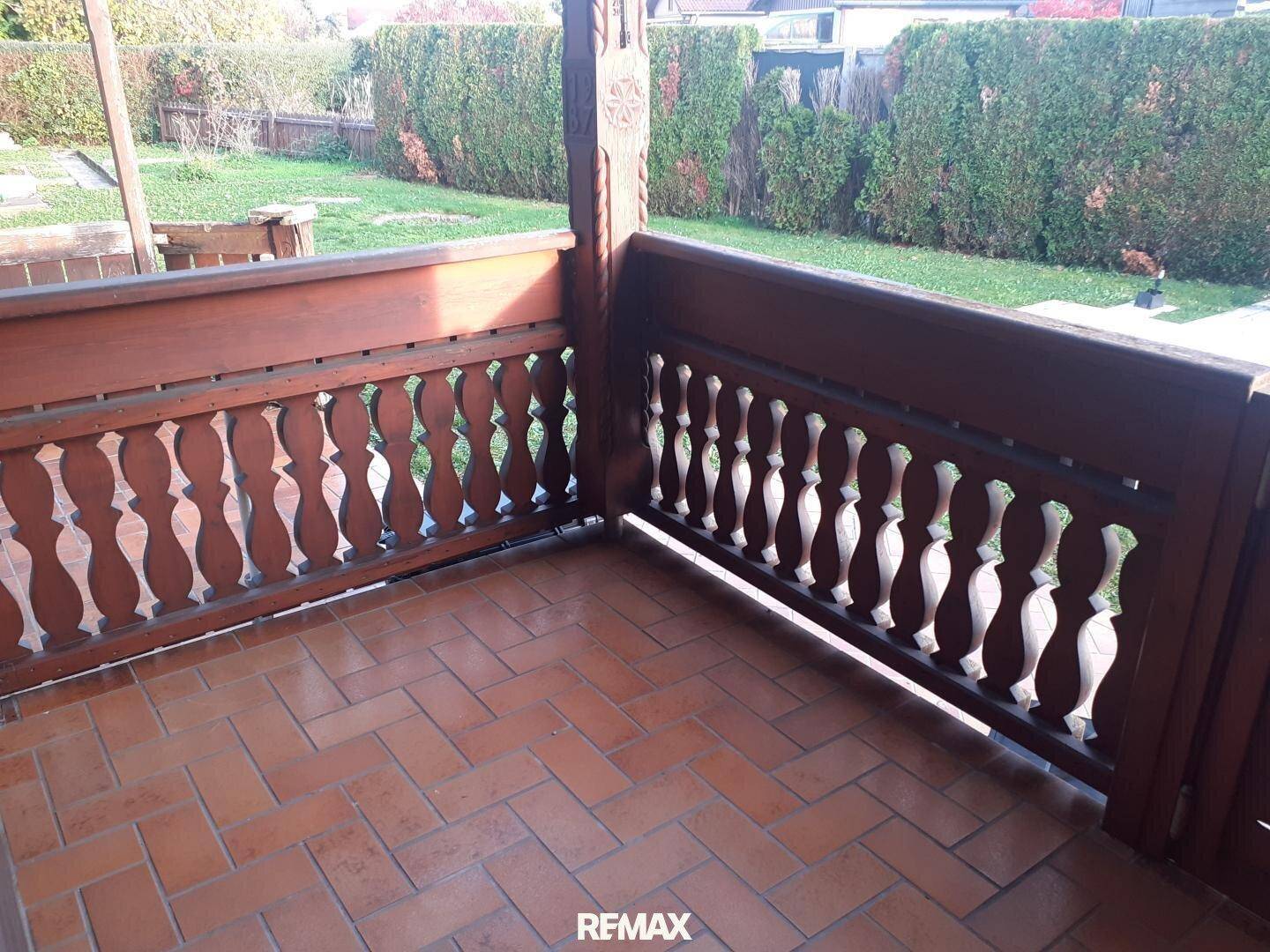 Traditioneller Holzbalkon mit geschnitztem Geländer und Blick ins Grüne.