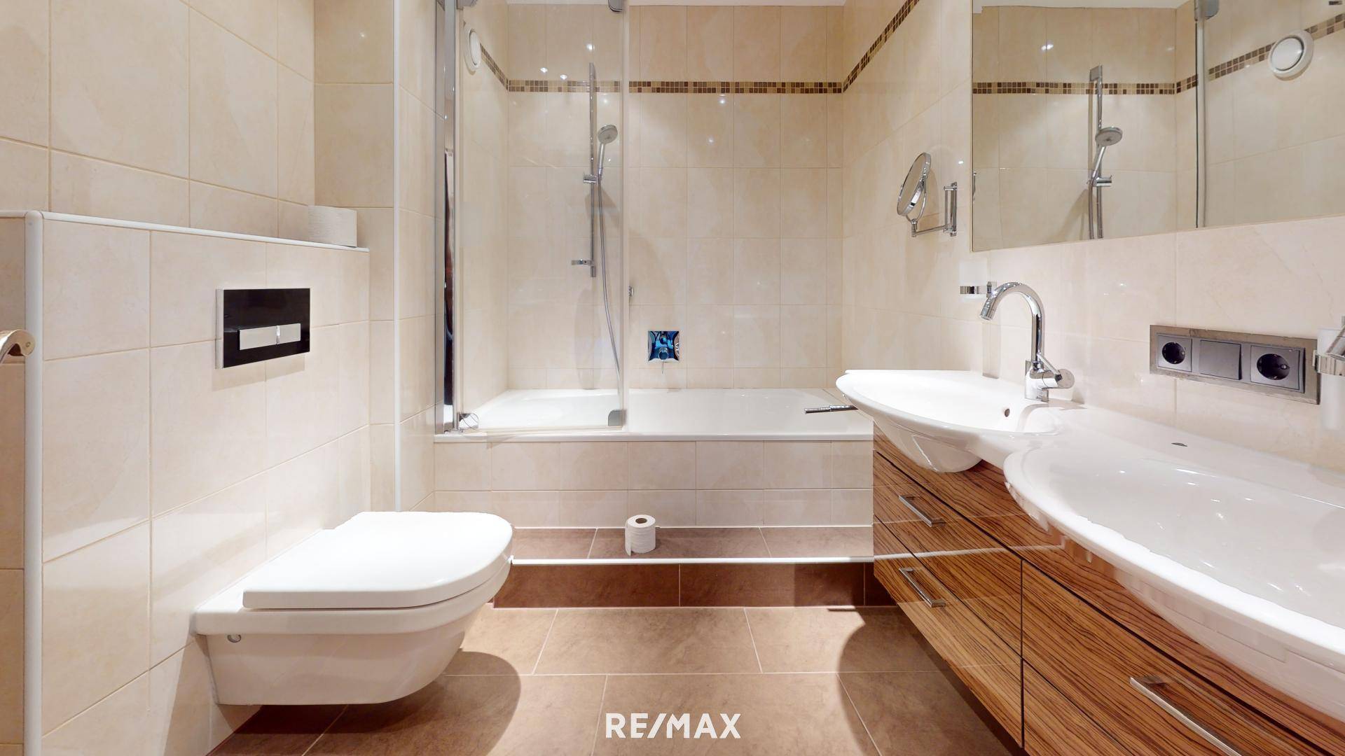 Modernes Badezimmer mit beigefarbenen Fliesen, Badewanne mit Duschwand und wandhängendem WC.