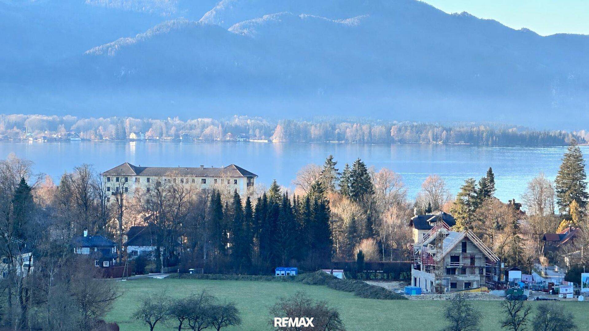 Weitläufiger Blick auf den See mit umliegenden Bergen und Häusern am Ufer.