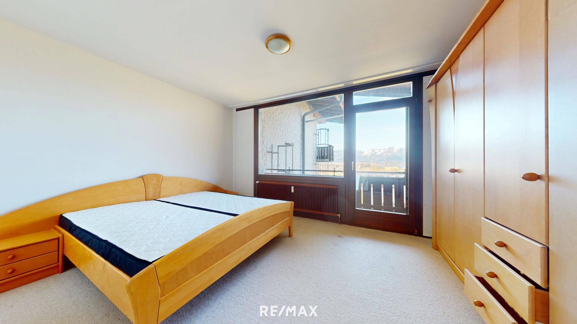 Helles Schlafzimmer mit Holzbett, Kleiderschrank und Zugang zu einem Balkon mit Bergblick.