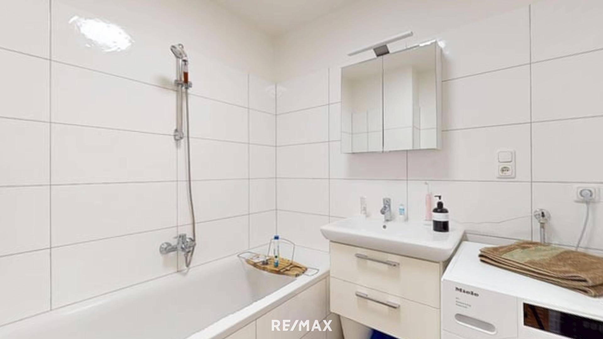 Funktionales Badezimmer mit Badewanne, Duschfunktion, Waschbecken und integrierter Waschmaschine.