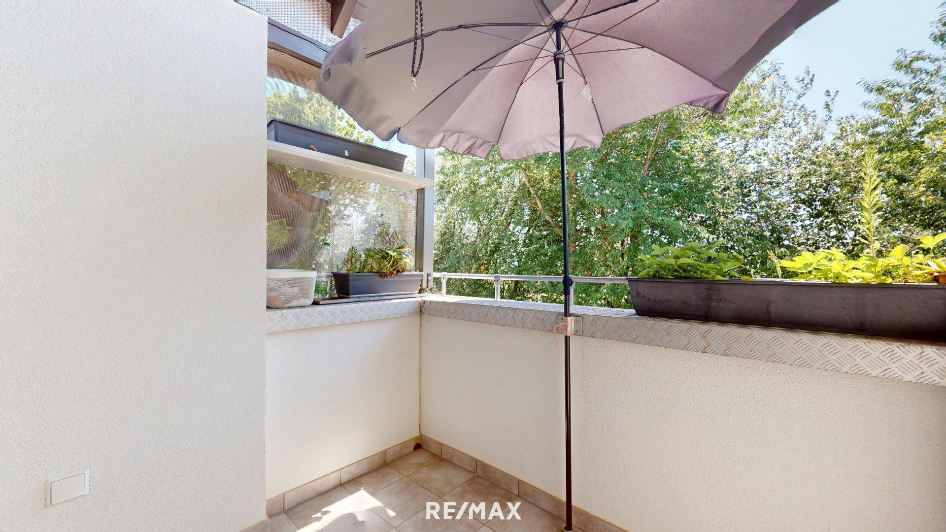 Gemütlicher Balkon mit Sonnenschirm, Pflanzen und Blick ins Grüne, ideal zum Entspannen.