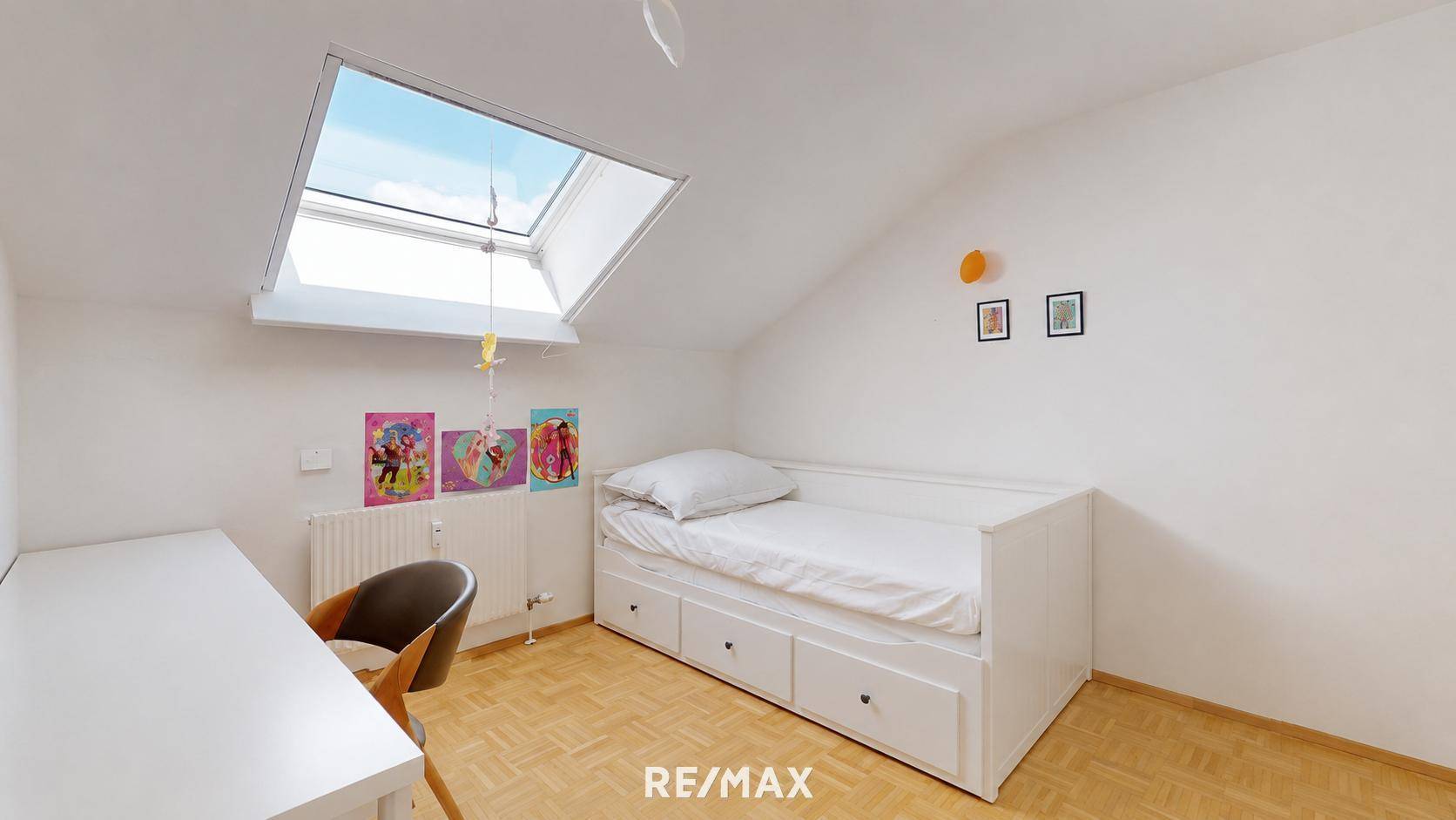 Helles Kinder- oder Gästezimmer mit Einzelbett, Schreibtisch und großem Dachfenster für viel Tageslicht.