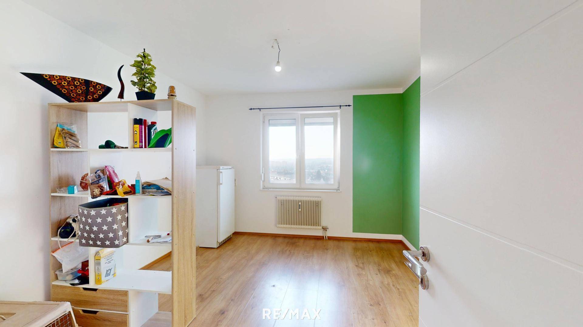 Heller Raum mit Holzboden, grüner Akzentwand und Fenster.