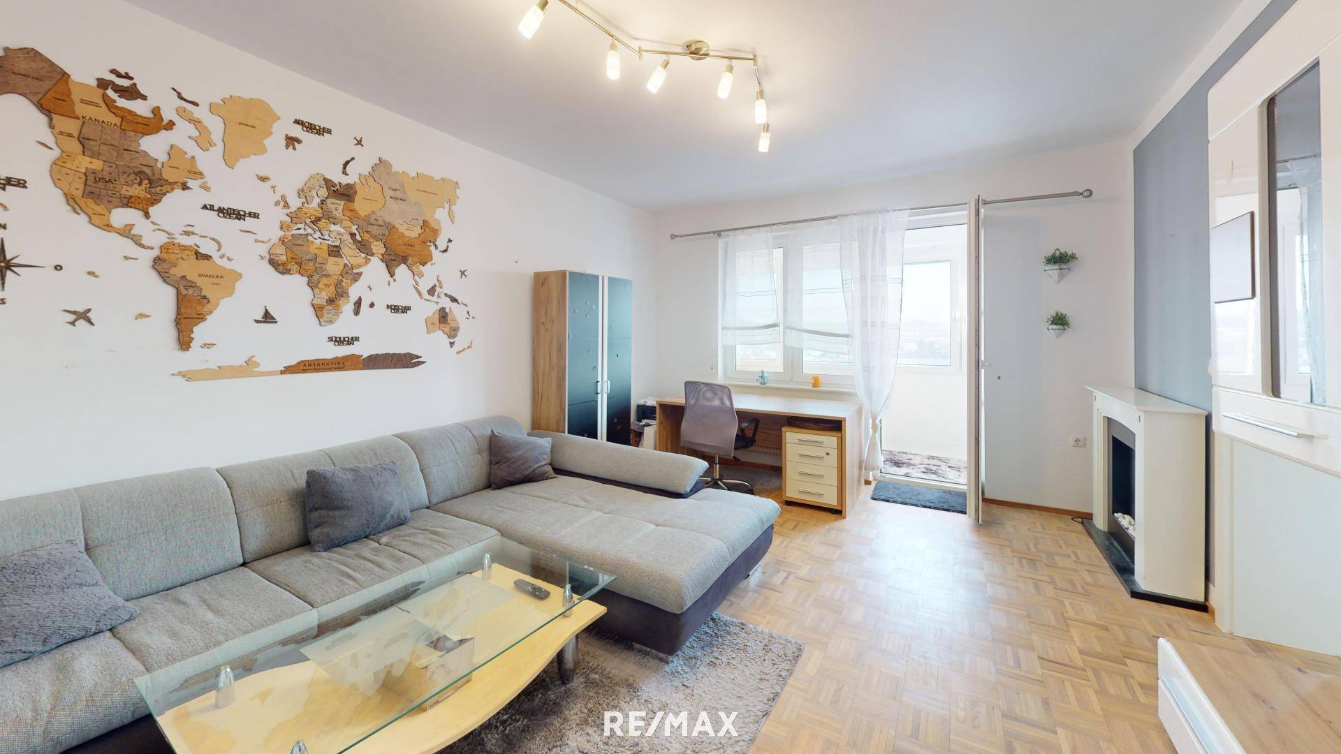 Gemütliches Wohnzimmer mit großem Sofa, Schreibtischbereich und Zugang zum Balkon.
