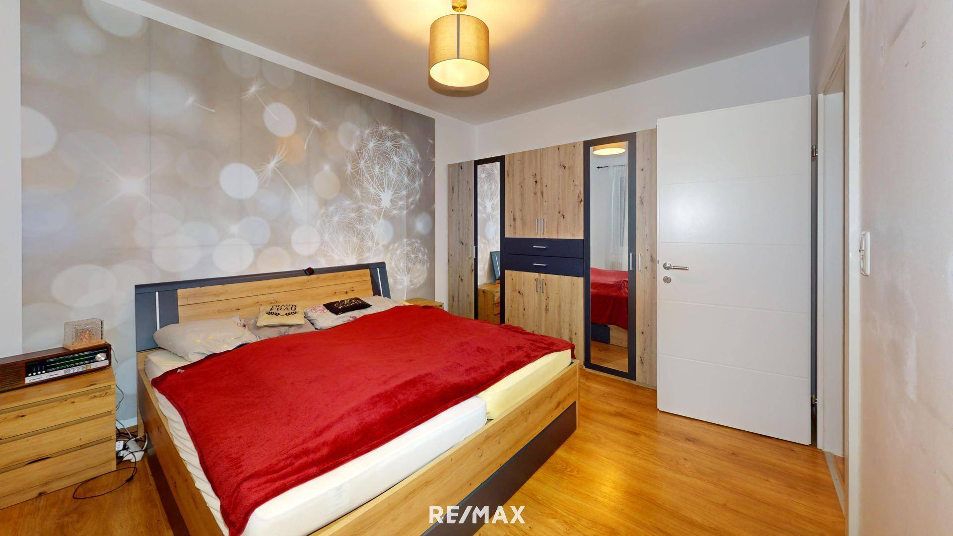 Schlafzimmer mit Doppelbett, Holzmöbeln und dekorativer Tapetenwand.