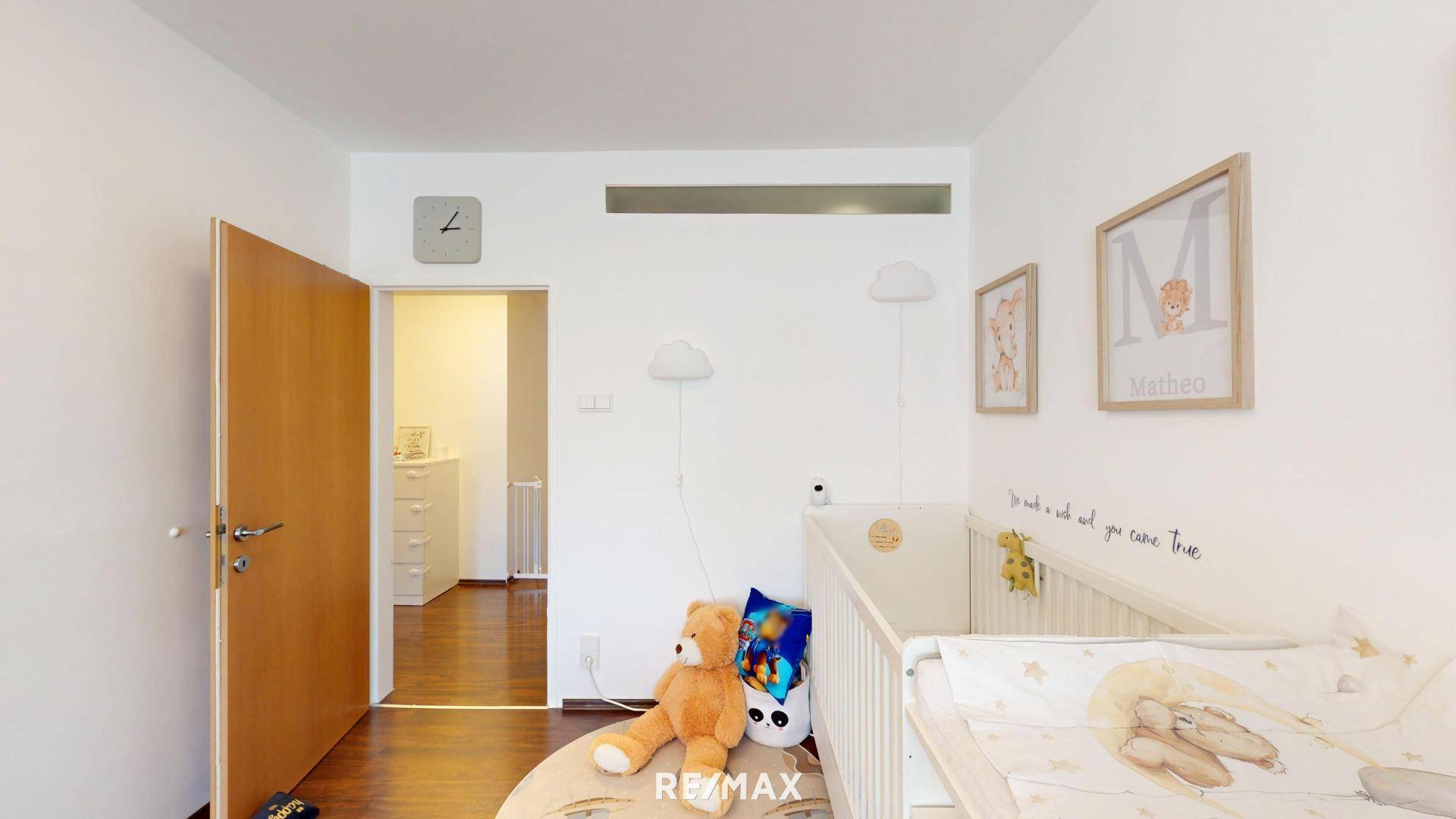 Kinderzimmer mit Babybett und Spielzeug, heller Raum mit Zugang zu einem weiteren Zimmer.