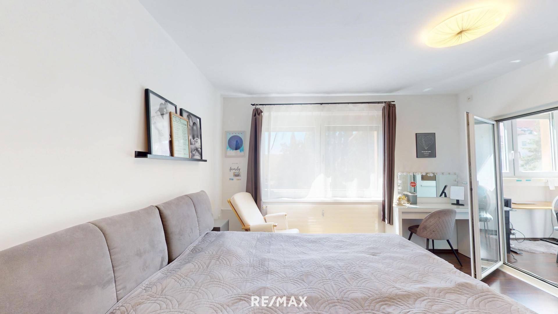 Schlafzimmer mit Bett, Sitzgelegenheit und einem Schminktisch am Fenster mit viel Licht.