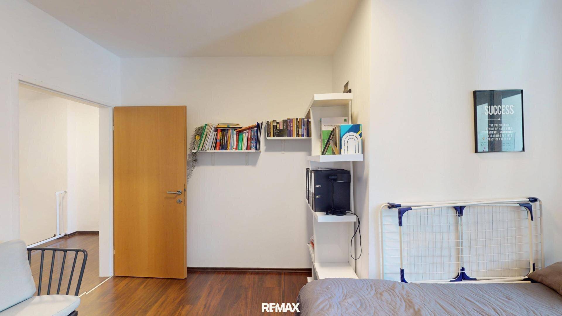 Schlafzimmer mit Bett, Bücherregalen und Zugang zu einem weiteren Raum, funktional eingerichtet.