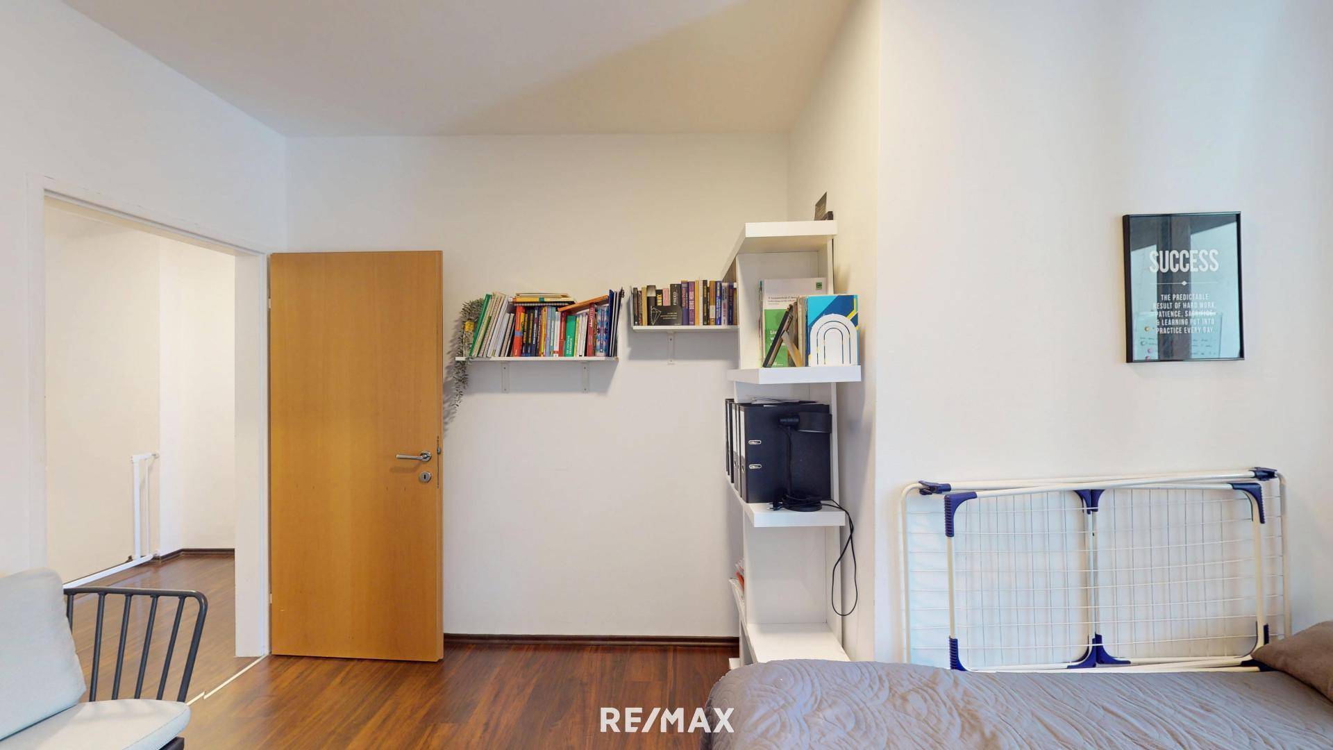 Schlafzimmer mit Bett, Bücherregalen und einer Tür, die zu einem anderen Raum führt.