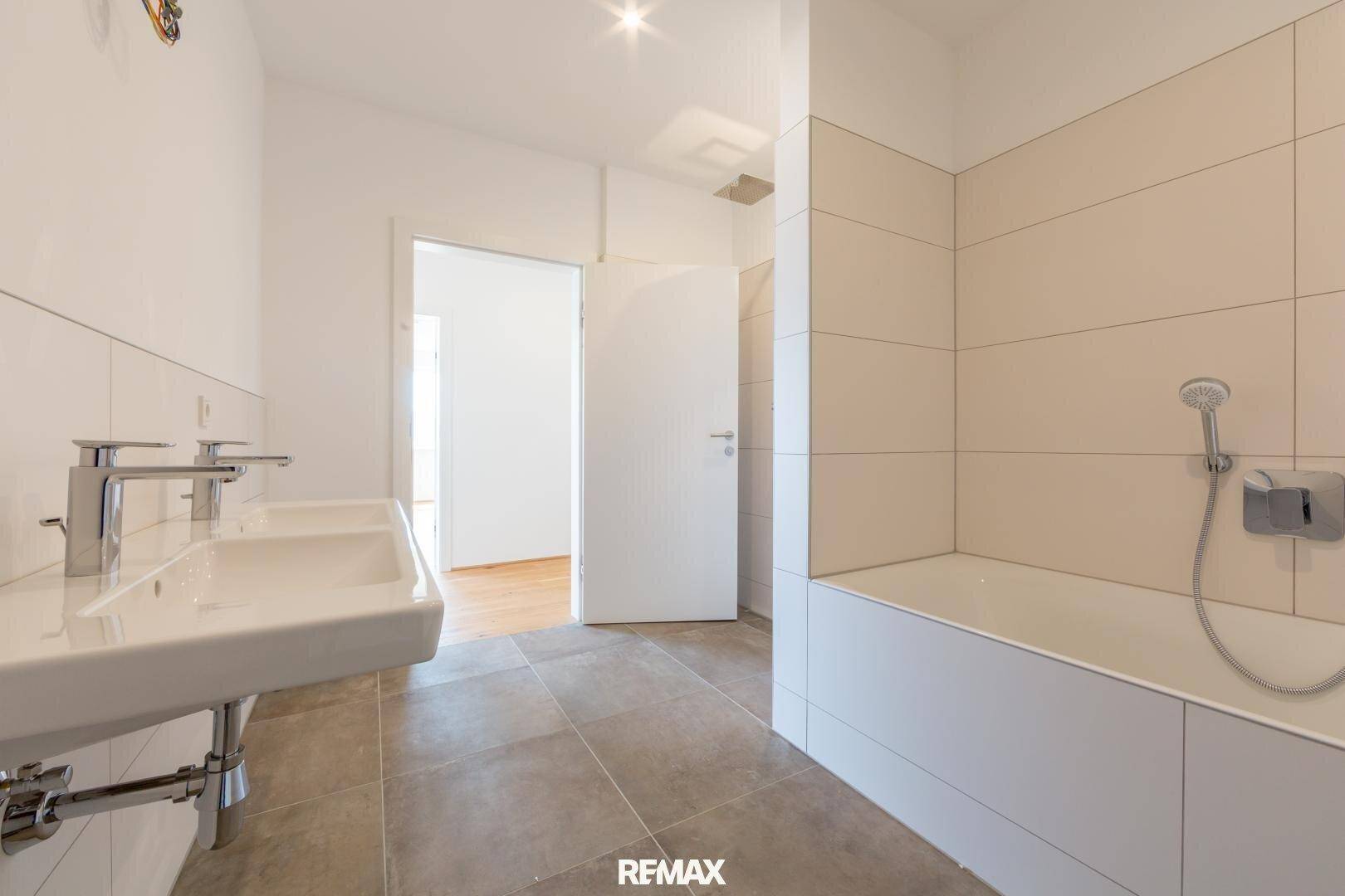 Modernes Badezimmer mit Doppelwaschbecken, Badewanne und hellen Fliesen.