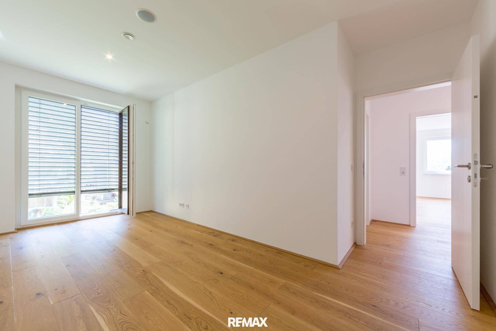 Helles Zimmer mit Holzboden und großem Fenster mit Jalousien, ideal als Schlafzimmer.