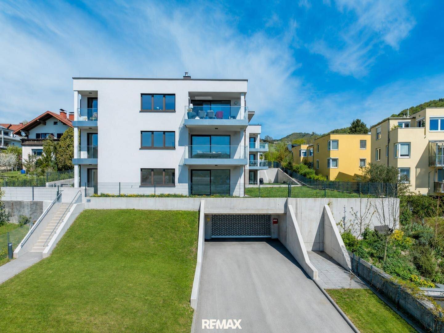 Modernes Mehrfamilienhaus mit Balkonen und Tiefgaragenzufahrt, umgeben von Grünflächen.