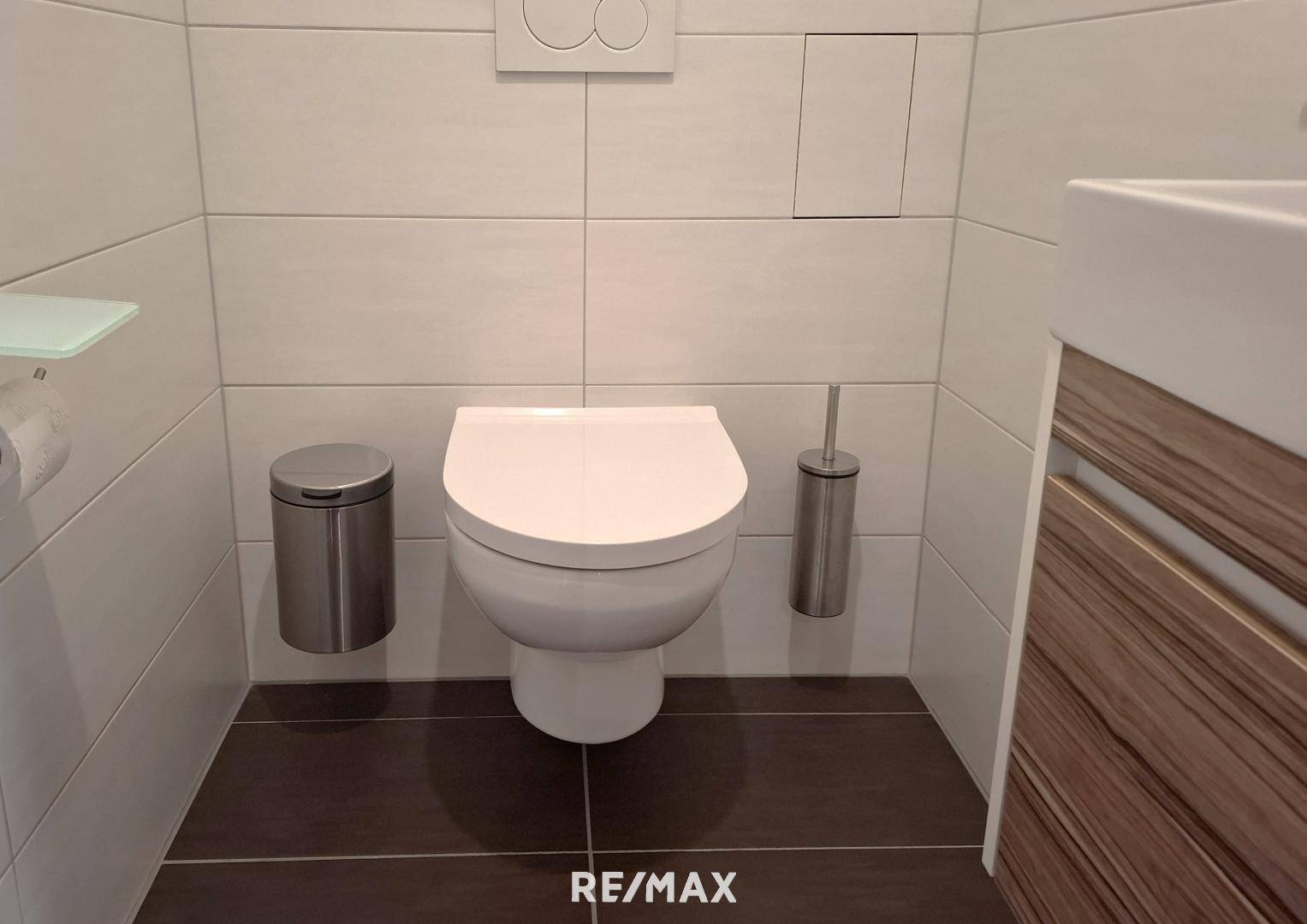 Gäste-WC mit wandhängender Toilette, kleinem Waschbecken und modernen Fliesen.