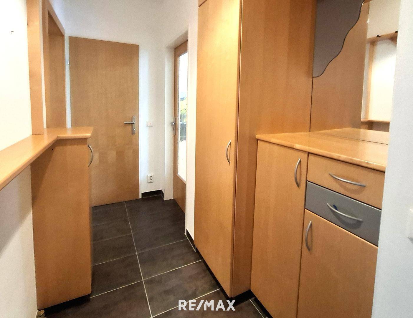 Heller Flur mit praktischen Einbauschränken aus Holz und dunklem Fliesenboden.