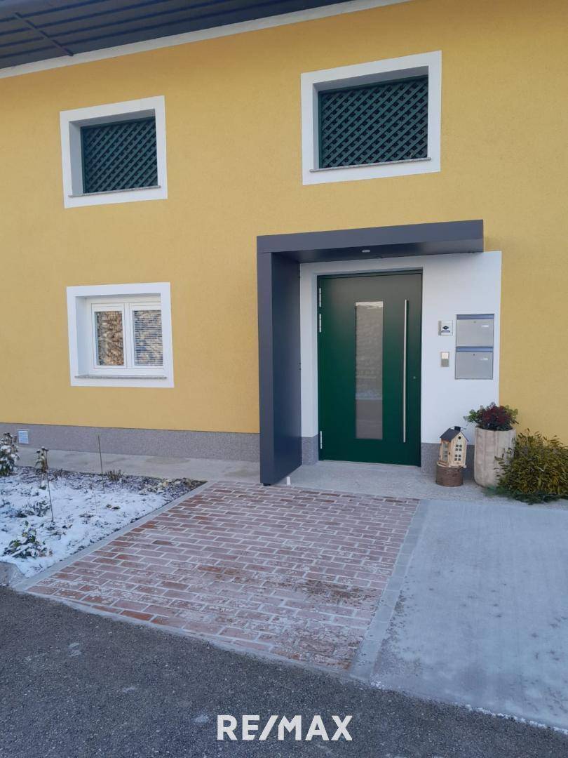 Gelbes Gebäude mit moderner grüner Eingangstür und gepflastertem Zugangsbereich im Winter.