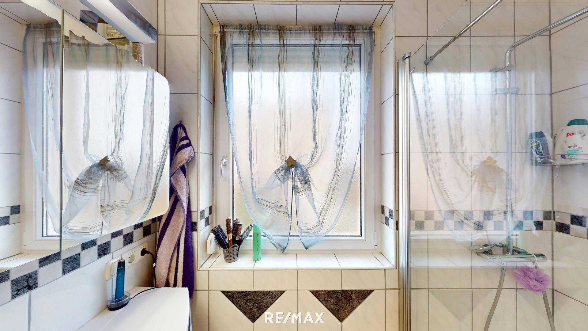 Badezimmer mit Duschkabine, Waschbecken, Spiegelschrank und einem Fenster.